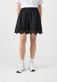 Černá sukně s elastickým pasem, vroubkovaným lemem a designem s laserem vypalovanými oky. Stylizováno s bílým tričkem a bílými teniskami.