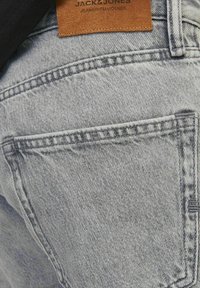  bolsillo trasero de unos vaqueros de mezclilla azul claro con costuras visibles y una etiqueta de cuero marrón que dice "JACK & JONES JEANS INTELLIGENCE."