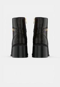 Botas pretas até ao tornozelo com um acabamento texturizado, um salto largo e acessórios em dourado. Apresenta um fecho de correr e um design com tiras cruzadas.