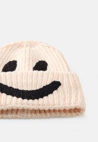 Stickad beanie i ljusrosa med svart smileyface-mönster; har ribbad textur, vikbar kant och mjukt, varmt tyg.