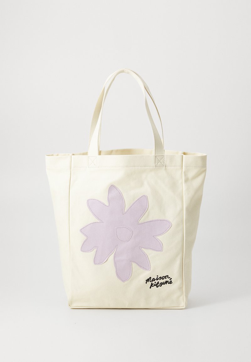 Canvas tote bag in cream with a large lavender flower appliqué and black "Maison Kitsuné" text. Features sturdy, flat handles.