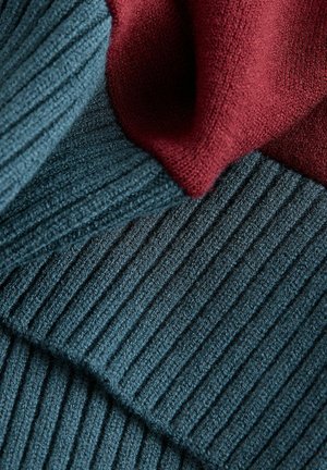 Gestrickter Stoff in Türkis mit vertikalem Rippenmuster, schichtweise mit einem weichen, glatten bordeauxfarbenen Textil kombiniert. Reiche Textur und kontrastierende Farben.