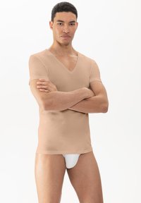 Licht beige V-hals T-shirt van textiel met een gestructureerde stof, korte mouwen en slanke pasvorm. Model poseert met gekruiste armen voor een effen achtergrond.