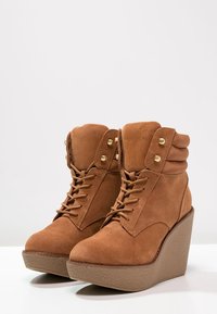 Brązowe zamszowe botki na klinie z teksturowaną platformą, okrągłym noskiem, sznurowanym zapięciem i złotymi akcentami metalowymi.