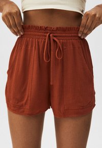 Shorts in Rostfarbe aus strukturiertem Stoff, mit elastischem Bund und verstellbarem Kordelzug. Verfügt über zwei seitliche Taschen für zusätzlichen Komfort.