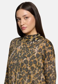 Sweter w panterkę, wykonany z miękkiej tkaniny. Posiada wysoki kołnierz i luźny krój. Paleta kolorów obejmuje odcienie czerni, złota i brązu.