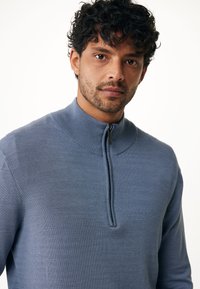 Ljusblå, zip-up tröja med hög krage, tillverkad av texturerad stickad tyg. Har en minimalistisk design och en tät passform.