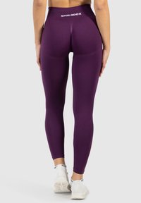 Leggings viola con vita alta, caratterizzati da un logo bianco sul retro. Il materiale appare liscio e aderente, con un design elegante.