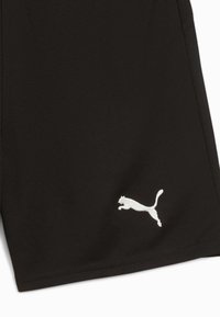Schwarzer Stoff mit weißem, gesticktem sprangenden Puma-Logo nahe dem unteren Rand, der einen Teil eines Kleidungsstücks zeigt.