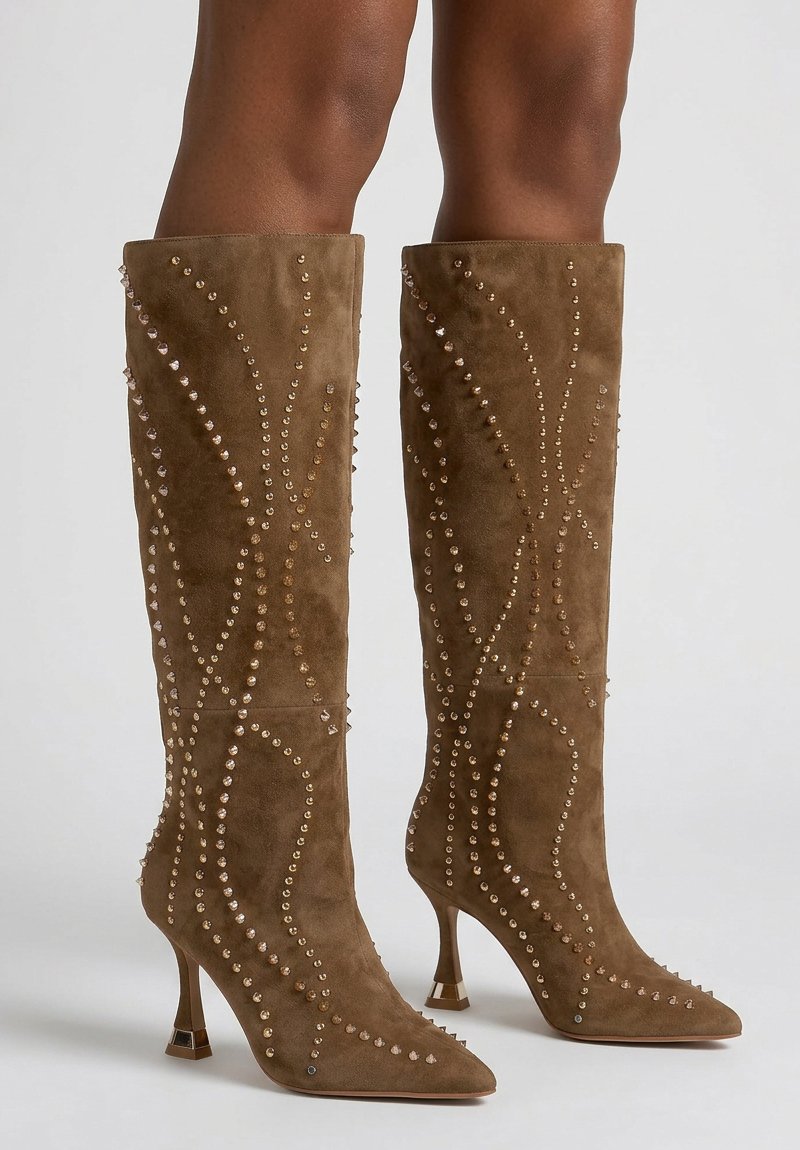 Bruine suède kniehoge laarzen met hoge hakken, versierd met gouden en zilveren studs langs de zijkanten en voorkant.