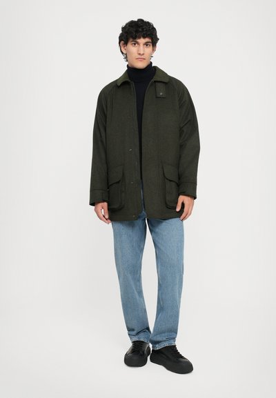 Olive green wool-blend jacket with a collar, front buttons, and two large pockets. Worn over a black turtleneck and light blue jeans.