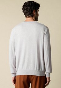 Svetle šedý svetr vyrobený z měkké látky, s dlouhými rukávy, žebrovaným lemem a manžetami a jednoduchým kulatým výstřihem.