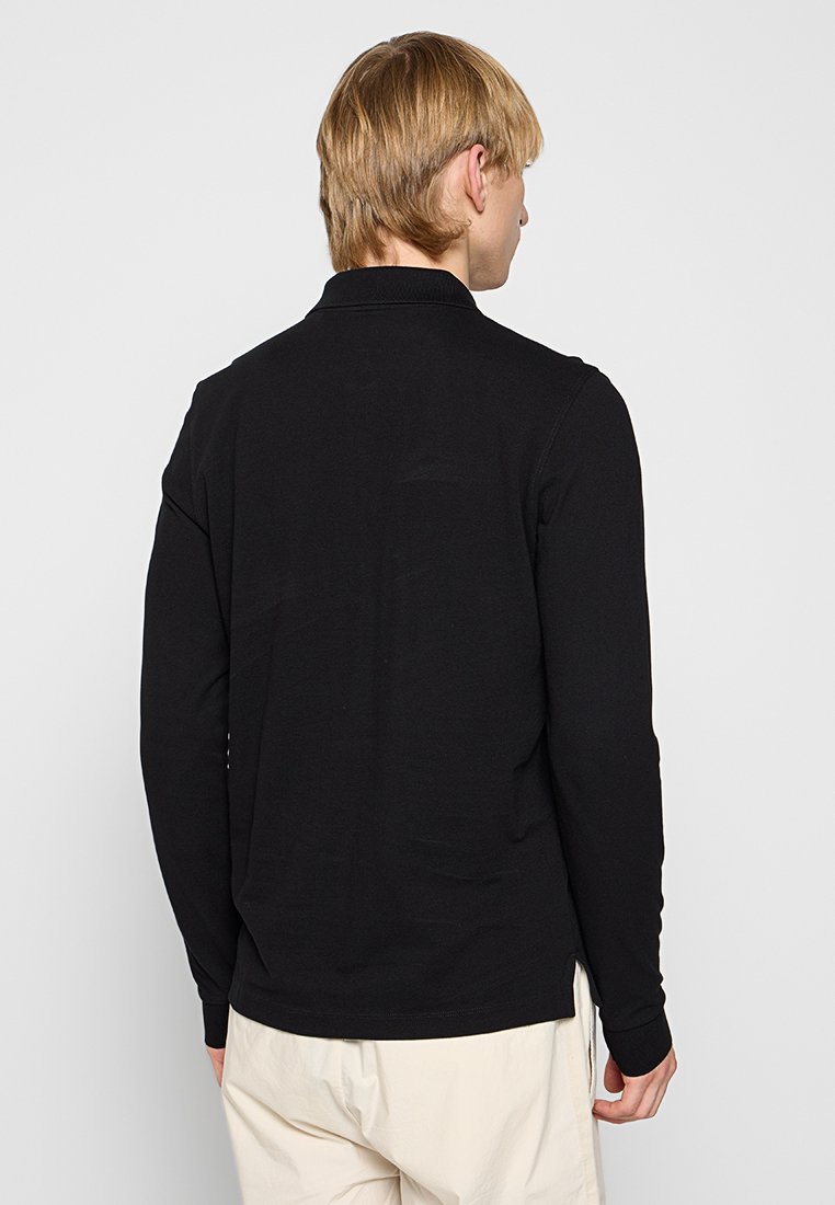 Czarna koszula polo z długim rękawem, o prostym dolnym brzegu i bocznych rozcięciach. Posiada klasyczny kołnierzyk i gładką teksturę. Minimalistyczny design.