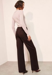 Svijetlosiva rebrasta pamučna majica s ovratnikom uparen je s tamnosmešnim širokim hlačama koje imaju stražne džepove i glatku teksturu.