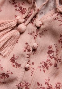 Lys rosa linnedragt med et blomsterprint i mørkerød. Inkluderer kvaster, rundede knapper og en bindelukning med stofdetaljer.
