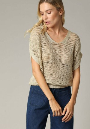 Beige, los gebreide trui met een V-hals en korte mouwen, gedragen over donkerblauwe spijkerbroeken. Kenmerkt zich door een open geweven textuur en een casual pasvorm.