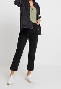 Chaqueta de mezclilla negra y jeans negros combinados con una blusa verde y zapatillas blancas. Los jeans tienen dobladillos enrollados y un corte relajado.