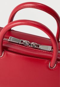 Κόκκινη δερμάτινη τσάντα χειρός με δύο στρογγυλεμένες λαβές και διπλό ασημένιο φερμουάρ στο πάνω μέρος, πάνω σε απλό φόντο.