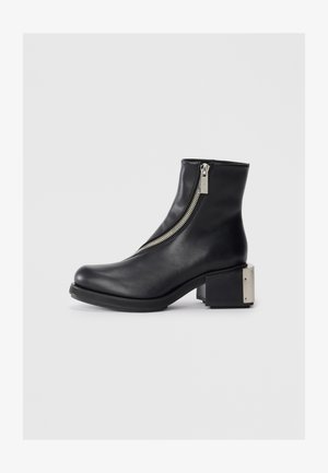 Must musta ankle boot, mille külgse tõmbega, kaarjas varvas ja blokk-kand, milles on metalliline aktsent. Sile tekstuur ja kaasaegne siluett.