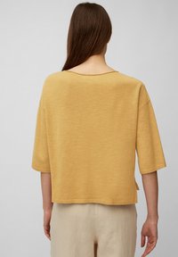Haut jaune à manches courtes avec un encolure large et une coupe décontractée, fabriqué en tissu léger, présente un ourlet droit avec des fentes latérales.