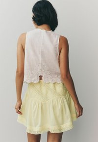 Un top court rose clair avec un ourlet festonné et une broderie florale, associé à une jupe jaune, superposée et texturée, avec des accents en dentelle.