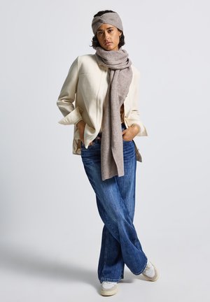 Beige blazer over a brown knit scarf and headband, paired with blue wide-leg jeans and light sneakers. Neutral color palette and soft textures.