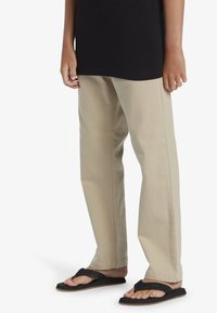 Beige katoen broek met een rechte pijp, gecombineerd met zwarte flip-flops en een zwart T-shirt dat zichtbaar is bij de taille.