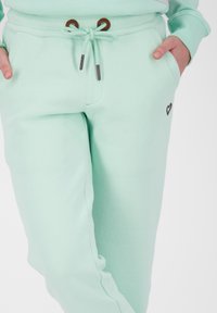 Mintgrön sweatpants i mjukt tyg, med dragsko i midjan med bruna detaljer och en liten hjärtlogotyp på vänster sida.