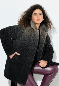 Tekokarhu takki, jossa on ombre-muotoilu, joka siirtyy tummasta mustasta vaaleaan harmaaseen. Varustettu leveällä kauluksella ja sivutaskuilla sekä teksturoidulla kankaalla.