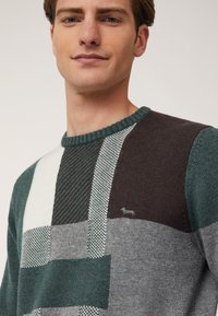 Maglione lavorato a maglia con scollatura a girocollo, caratterizzato da un design a patchwork in verde scuro, grigio, bianco e marrone, con un piccolo logo sul petto.