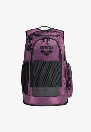 Mochila de nylon morada con detalles de malla, acentos negros, múltiples cremalleras y un logotipo. Cuenta con un asa superior y bolsillos laterales para almacenamiento.
