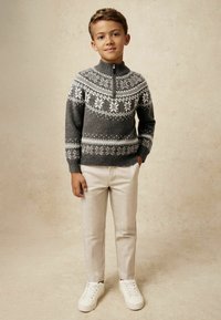 Maglione grigio a maglia con motivi di fiocchi di neve bianchi, colletto con zip, abbinato a pantaloni beige e sneaker bianche. Tessuto liscio e design aderente.