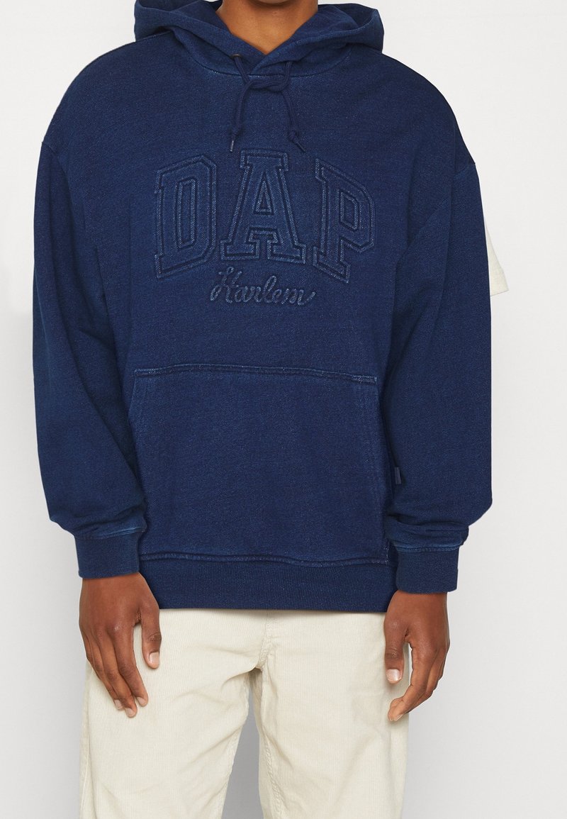 Dunkelblaues Kapuzensweatshirt mit weicher Textur, ausgestattet mit gesticktem "DAP"-Logo und "Harlem" in kontrastierendem Design. Vordertasche vorhanden.