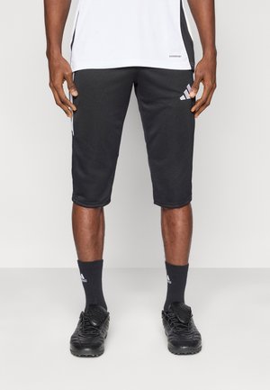 Zwarte atletiekshorts met een gladde textuur, witte zijstrepen en een Adidas-logo op het linkerbeen, gecombineerd met zwarte voetbalschoenen en sokken.