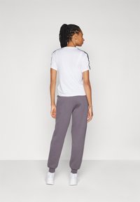 Hvit kortermet skjorte med svarte sidestriper, kombinert med grå joggebukser med nederste kant og avslappet passform. Hvite joggesko fullfører antrekket.