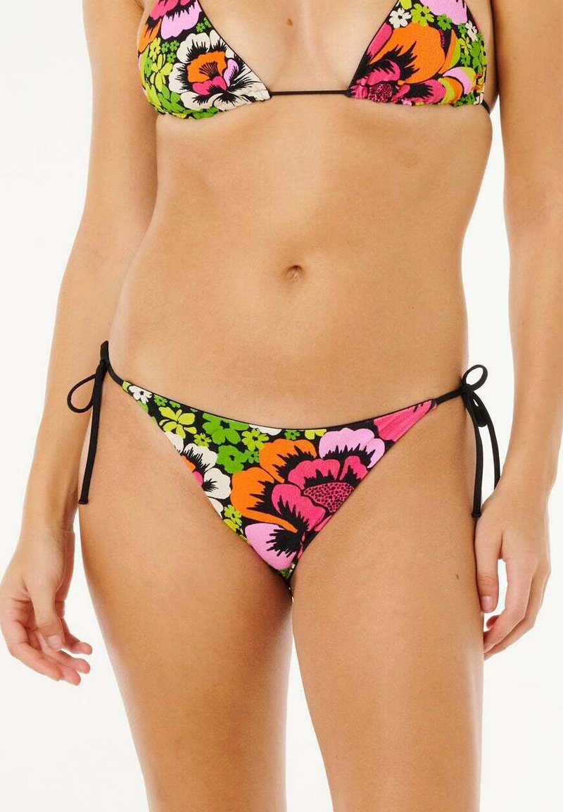 Frau trägt einen geblümten Bikini mit leuchtend orangen, pinken, weißen und grünen Blumen und schwarzen Schnürungen an Hüfte und Hals.