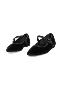 Zapatos de terciopelo negro con puntas afiladas, con un diseño de tiras cruzadas y un detalle de hebilla ajustable. Textura suave y suelas planas.