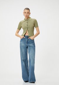 Top verde a maniche corte in maglia ribbed con colletto e chiusura a bottoni, abbinato a jeans in denim blu a vita alta e gamba larga.