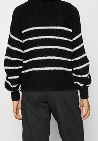 Schwarz-weißer gestreifter Pullover mit einem groben Stricktextur, lockerer Passform und gerippte Bündchen. Hat einen hohen Kragen und überschnittene Schultern.