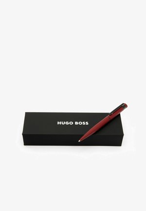 Rode slanke pen met een zwarte clip rustend op een zwarte doos met witte "HUGO BOSS" branding. De doos is rechthoekig en minimalistisch.