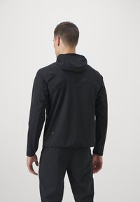 Schwarze Kapuzenjacke mit schickem Design, langen Ärmeln, einem Rückenschlitz und einem Logo am unteren Saum. Leicht und mit glatter Textur.