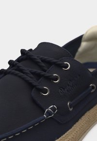 Ναυτικό μπλε καστόρινο παπούτσι για βάρκα με πλεκτά κορδόνια, μεταλλικά ρουθούνια, ραφές διακόσμησης και πλεγμένη άκρη σόλας από γιούτα.