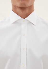 Witte overhemd met een klassieke kraag, zes knopen aan de voorzijde, gladde textuur en getailleerd ontwerp. Geen zichtbare patronen of accenten.