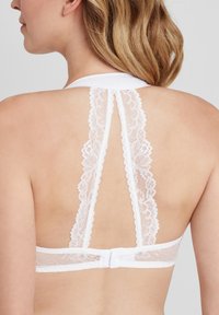 Weiße Spitzen-Bralette mit Racerback-Design und gewelltem Spitzenbesatz. Rückenverschluss mit verstellbaren Trägern. Glatte Stoffstruktur.