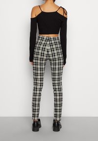 Haut noir à manches longues raccourci avec détail épaules dénudées, associé à un pantalon taille haute à carreaux noir et blanc et des chaussures noires.