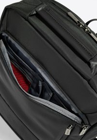 Zaino nero con un'esterno texturizzato, diversi scomparti con zip e un interno con rivestimenti in tessuto grigio e rosso.