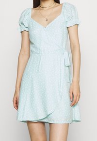 Ljusblå omslagsklänning med korta puffärmar, blommönster, V-ringning, justerbar knytning i midjan och utsvängd fåll.