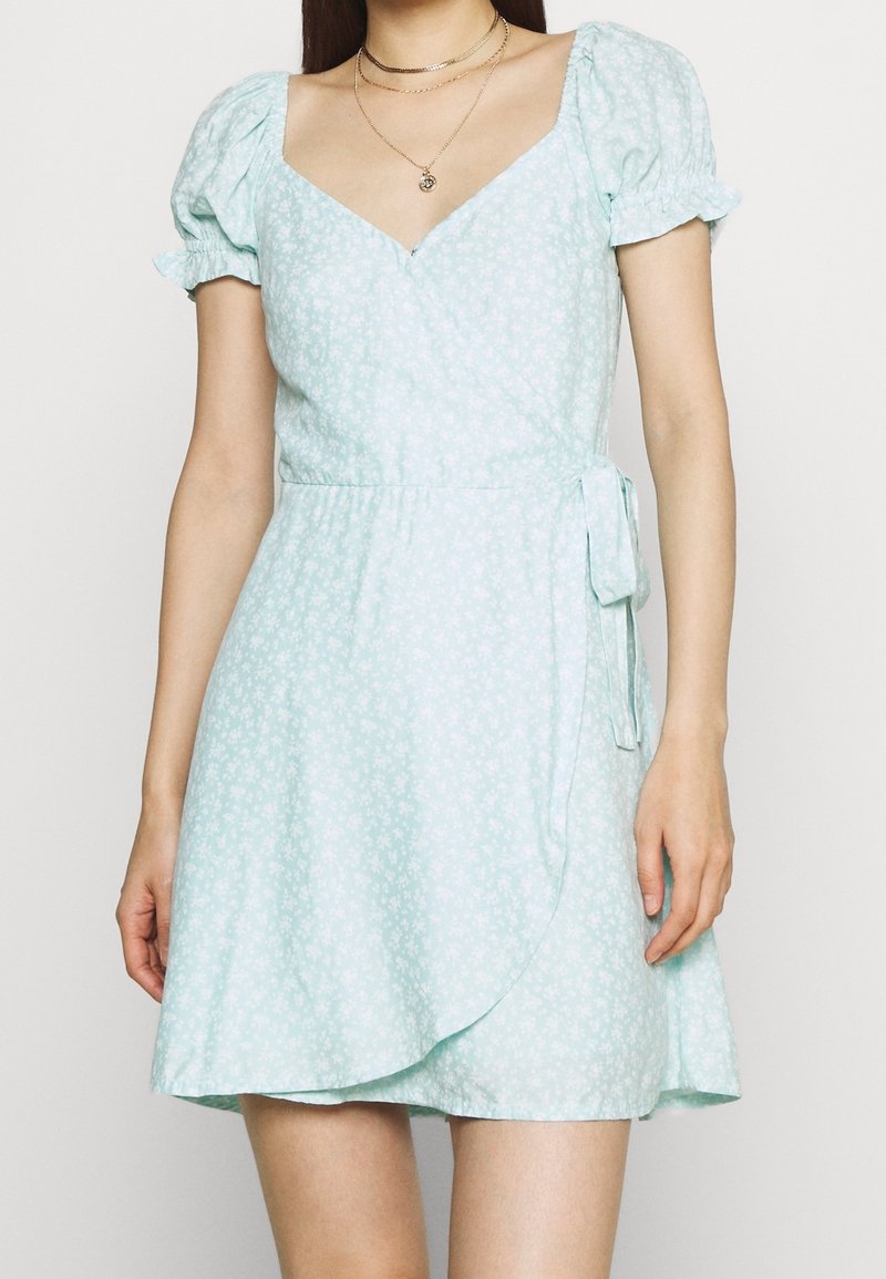 Ljusblå omslagsklänning med korta puffärmar, blommönster, V-ringning, justerbar knytning i midjan och utsvängd fåll.