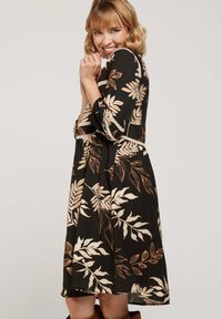 Robe noire avec un motif de feuilles beiges, manches trois-quarts, taille cintrée et tissu texturé, dotée d'un passepoil décoratif blanc.
