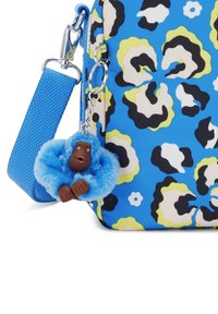 Blaue, mit Blumenmuster verzierte Tasche mit einer Kettenriemen. Sie hat einen flauschigen blauen Affen-Schlüsselanhänger mit einem braunen Gesicht, krallenartigen Händen und ausdrucksvollen Merkmalen.